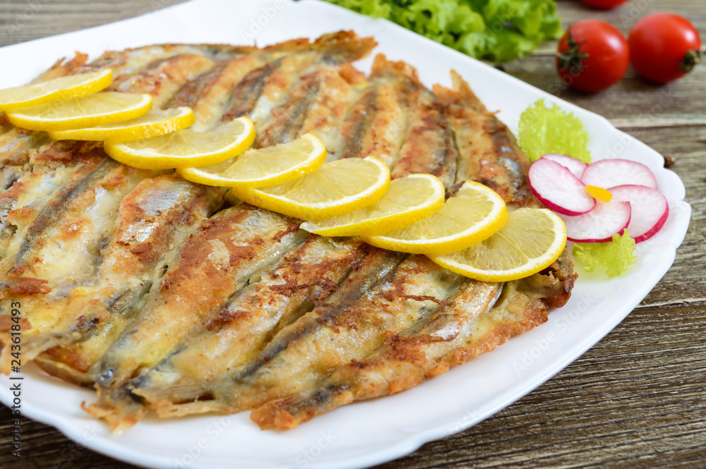 Baked capelin on a white plate on a wooden table. A dish of small fish Baked capelin on a white plate on a wooden table. A dish of small fish