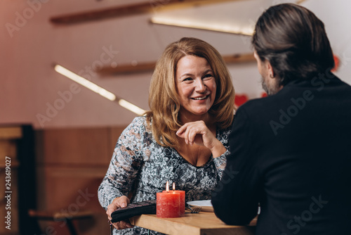A middle-aged couple at a table in a cafe on Valentine's Day. Focus on a smiling blonde woman