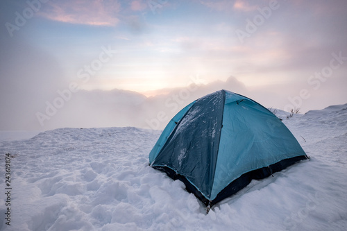 Camping blue tent at snowy hill in foggy