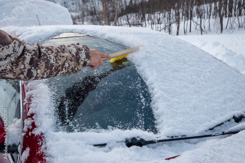 Hand using brush sweeping snow on car windscreen
