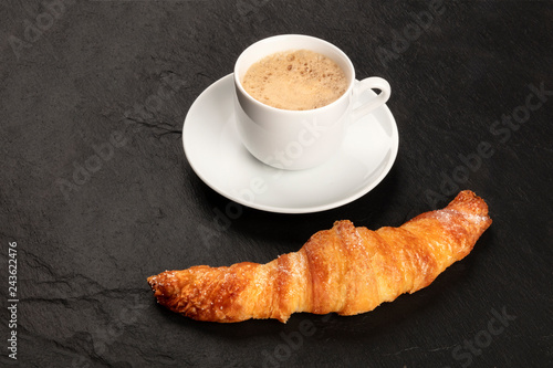 A photo of a croissant with a cup of coffee on a black background with copy space