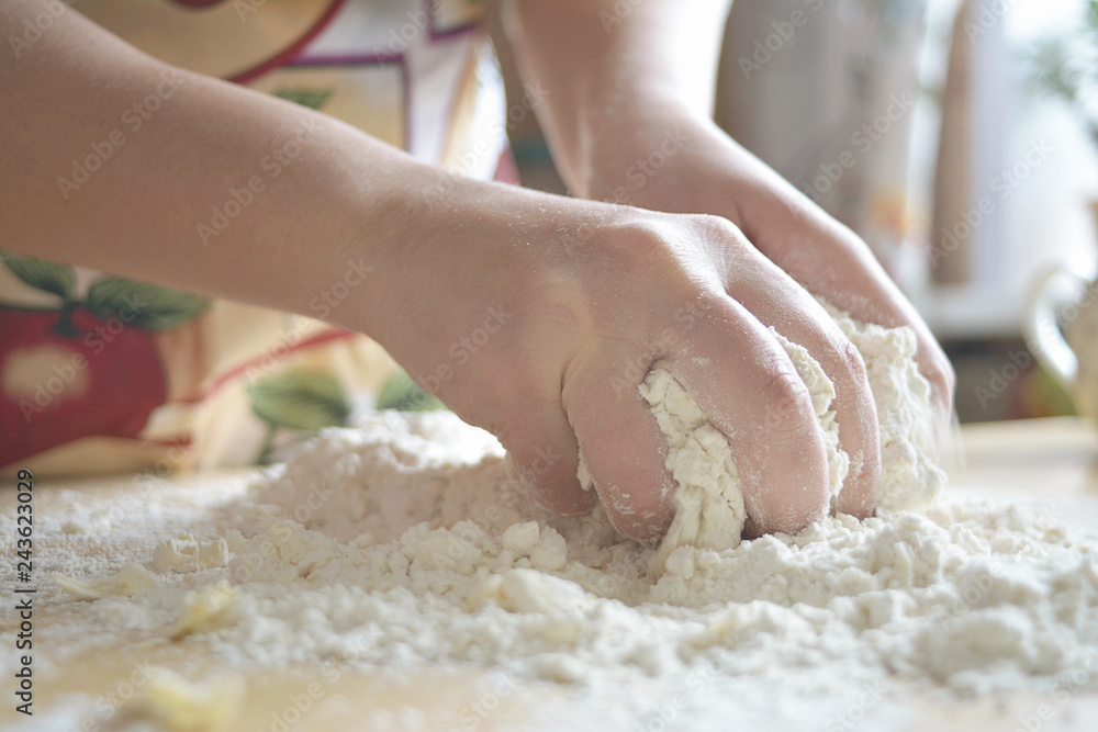 A woman in a colored apron kneads dough on the table. A woman in a colored apron kneads dough on the table.