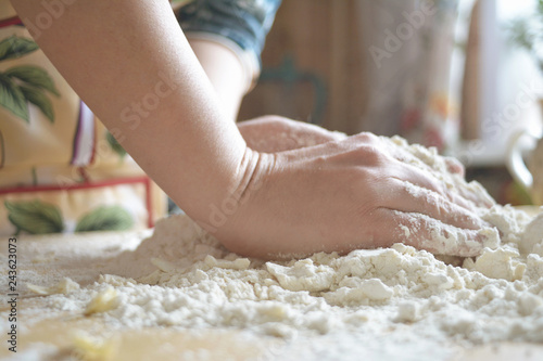 A woman in a colored apron kneads dough on the table.