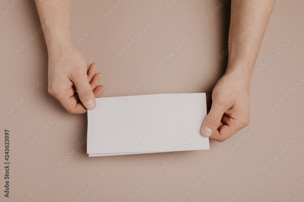 Man holds a mock-up letter or postcard in his hands with envelope on a gray background Man holds a mock-up letter or postcard in his hands with envelope on a gray background