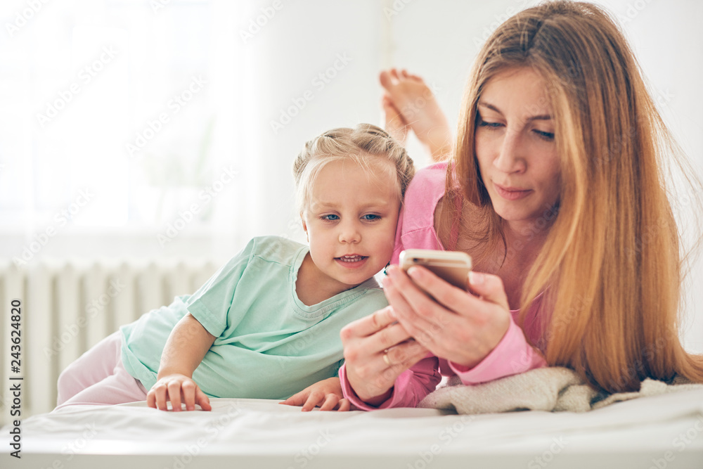 Young mother and her baby daughter using smart phone in bed Young mother and her baby daughter using smart phone in bed