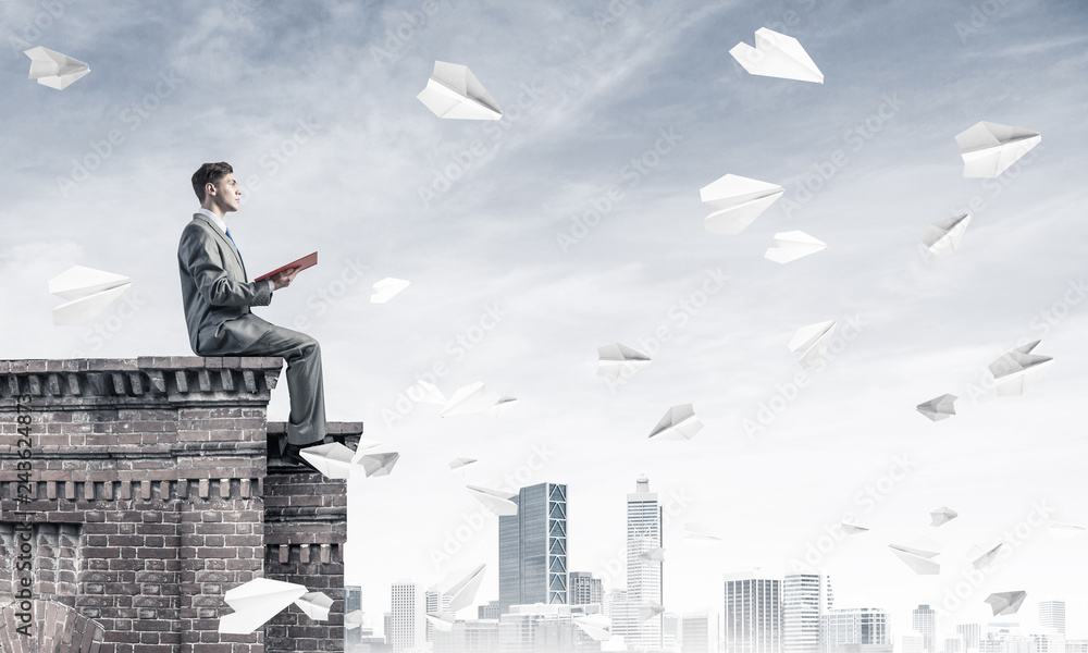 Man on roof edge reading book and cityscape at background Man on roof edge reading book and cityscape at background