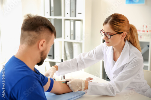 Female doctor drawing a blood sample of male patient in clinic