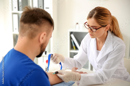 Female doctor drawing a blood sample of male patient in clinic