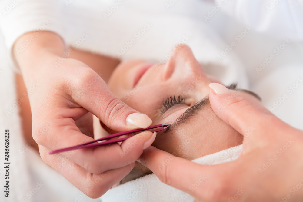 Beautician plucking eyebrows with tweezers of a woman in beauty salon Beautician plucking eyebrows with tweezers of a woman in beauty salon