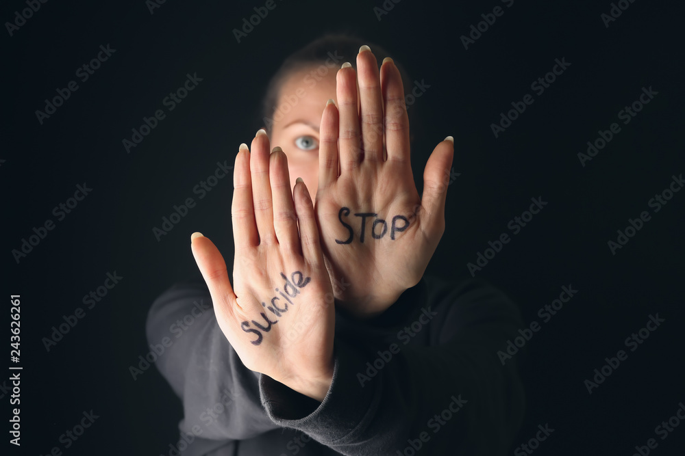 Text STOP SUICIDE written on palms of woman against dark background Text STOP SUICIDE written on palms of woman against dark background