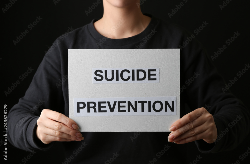 Woman holding paper sheet with text SUICIDE PREVENTION on dark background Woman holding paper sheet with text SUICIDE PREVENTION on dark background