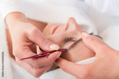 Beautician plucking eyebrows with tweezers of a woman in beauty salon