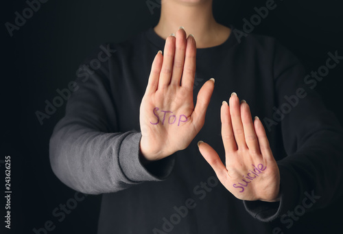 Text STOP SUICIDE written on palms of woman against dark background