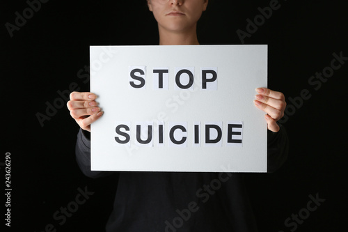 Woman holding paper sheet with text STOP SUICIDE on dark background