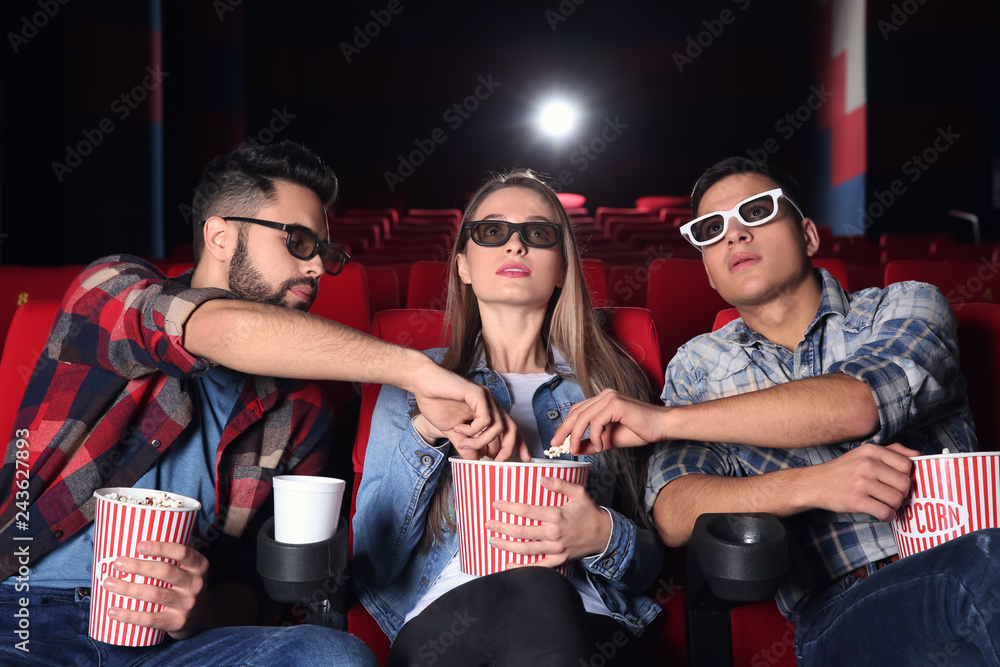 Fototapeta premium Guys eating popcorn from their friend's bucket in cinema