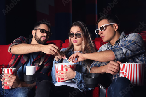 Guys eating popcorn from their friend's bucket in cinema