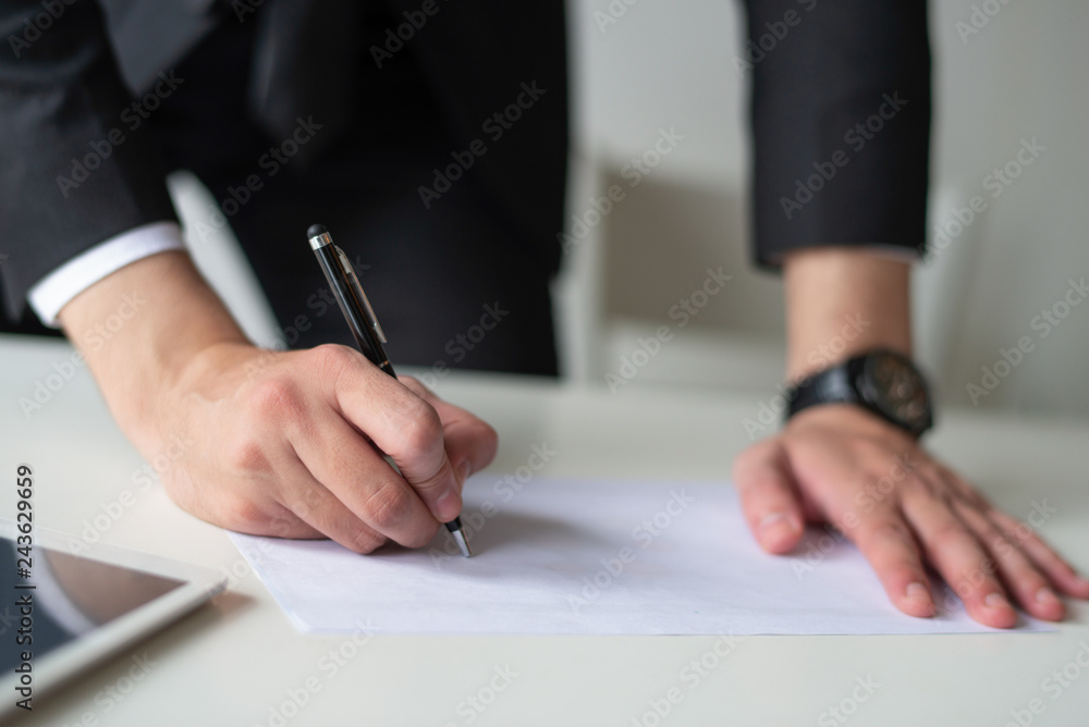 Closeup of business man making notes on sheet of paper at desk. Entrepreneur standing and working at office desk. Paperwork concept. Cropped view. Closeup of business man making notes on sheet of paper at desk. Entrepreneur standing and working at office desk. Paperwork concept. Cropped view.