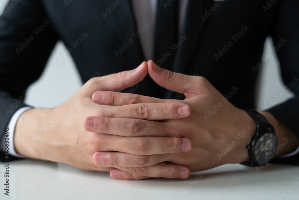 Closeup of pensive entrepreneur with clasped hands. Business man wearing suit and watch. Contemplation or waiting concept. Cropped front view.