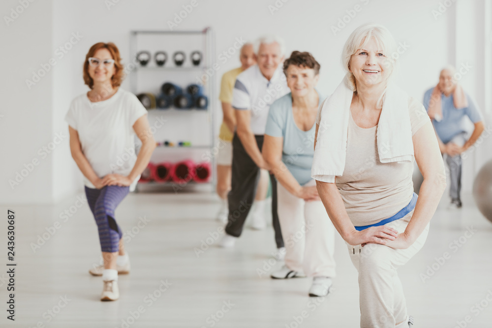 Smiling senior woman exercising with group of active seniors in fitness center - obrazy, fototapety, plakaty 