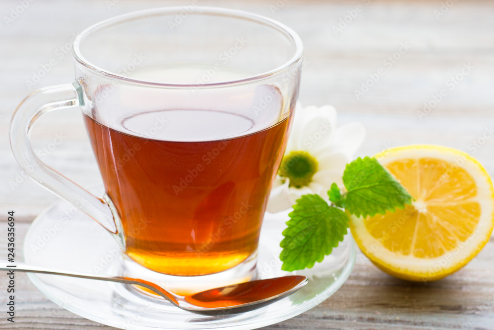 Black tea ceremony - glass full of tea, sugar, yellow lemon, tea leaves, spices on a wooden boards background Black tea ceremony - glass full of tea, sugar, yellow lemon, tea leaves, spices on a wooden boards background