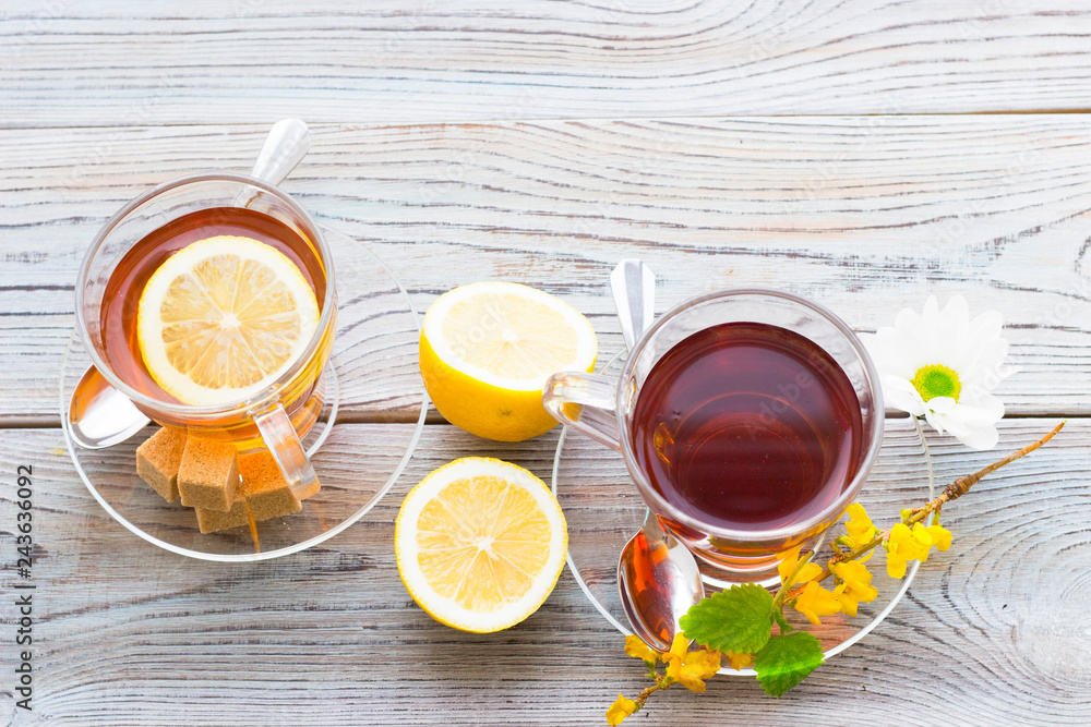 Black tea ceremony - glass full of tea, sugar, yellow lemon, tea leaves, spices on a wooden boards background Black tea ceremony - glass full of tea, sugar, yellow lemon, tea leaves, spices on a wooden boards background