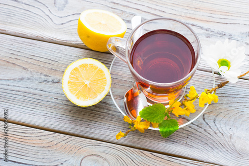 Black tea ceremony - glass full of tea, sugar, yellow lemon, tea leaves, spices on a wooden boards background