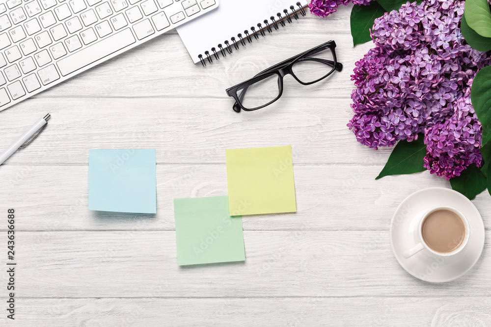 Office desktop with a bouquet of lilacs, coffee cup, keyboard, notebook and colored stickers on white boards Office desktop with a bouquet of lilacs, coffee cup, keyboard, notebook and colored stickers on white boards