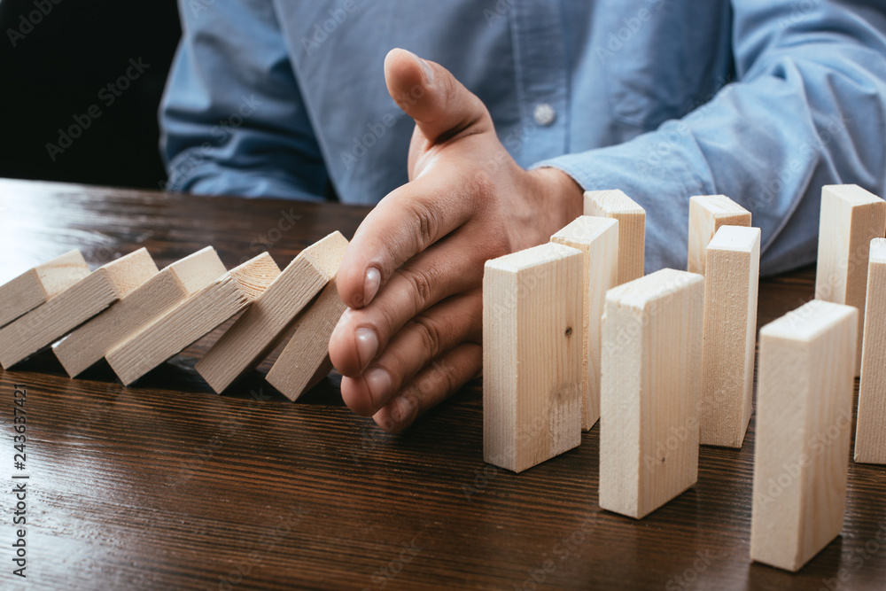 cropped view of man preventing wooden blocks from falling on desk cropped view of man preventing wooden blocks from falling on desk