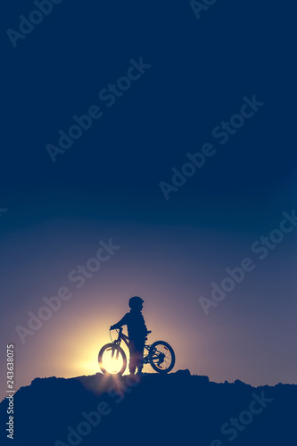 Silhouette of a little girl with a bicycle at sunset