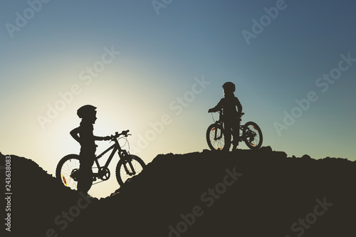 Silhouette of two little girls with bicycles at sunset