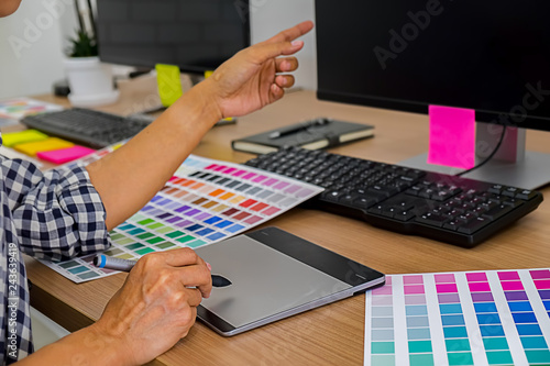 Graphic design with color swatches and tablet on a desk. Graphic designer drawing something on tablet at the office with work tools and accessories.