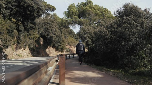 The guy with backpack walks on a footpath along the road in Barcelona