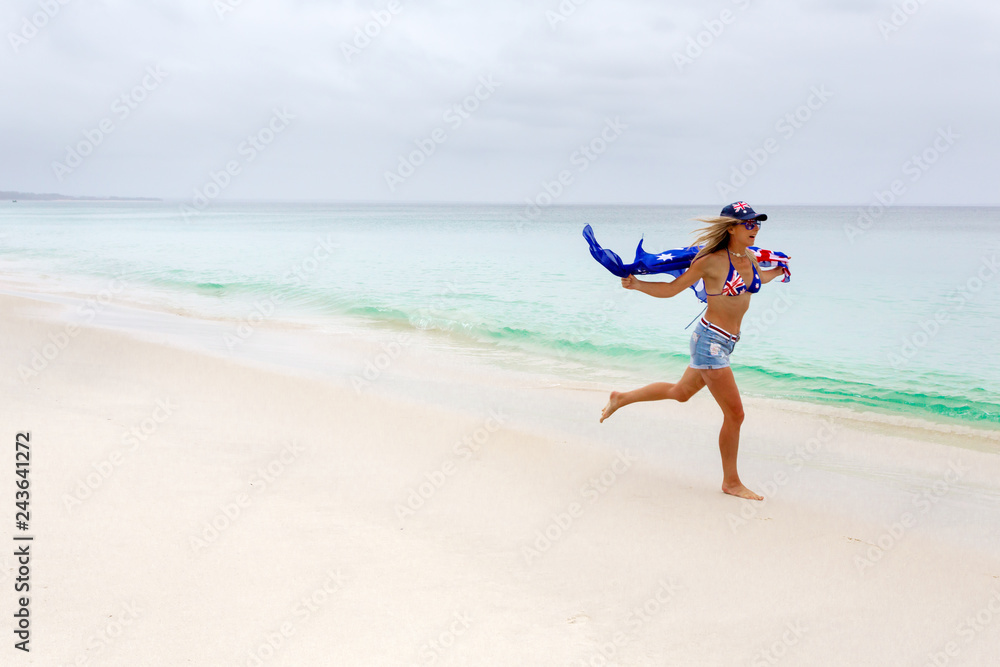 Australian woman running along the beach.  She has the Australian flag printed on her cossie and hat.  Some motion in woman