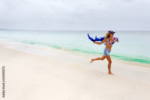 Australian woman running along the beach. She has the Australian flag printed on her cossie and hat. Some motion in woman