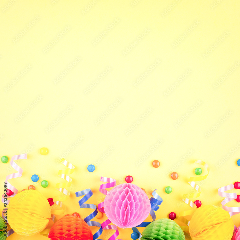 Obraz premium Birthday party background on yellow. Top view. Border made of colorful serpentine, balls and candies.