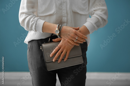 Beautiful young woman with stylish bijouterie and bag on color background