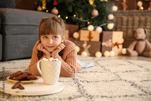 Cute little girl with hot chocolate and cookies at home on Christmas eve