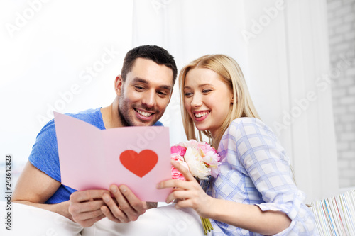 love, valentines day and people concept - happy couple with greeting card and flowers at home