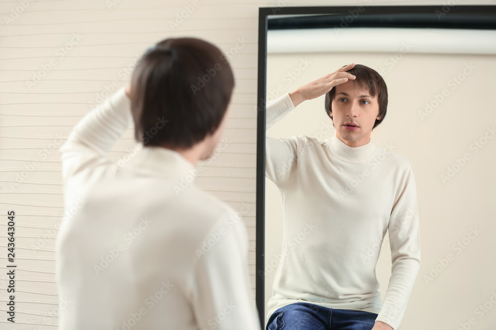 Young transgender man looking on his reflection in mirror Young transgender man looking on his reflection in mirror