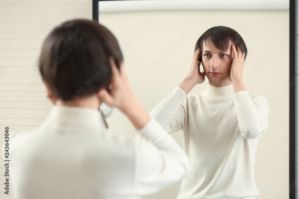 Young transgender man looking on his reflection in mirror Young transgender man looking on his reflection in mirror