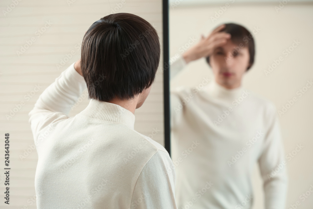 Young transgender man looking on his reflection in mirror Young transgender man looking on his reflection in mirror