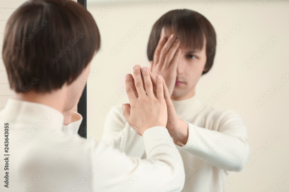 Displeased transgender man looking on his reflection in mirror Displeased transgender man looking on his reflection in mirror