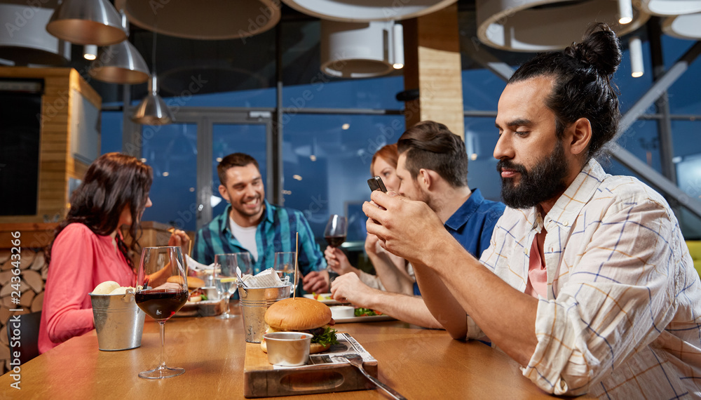 technology, lifestyle and people concept - man dining with friends and messaging on smartphone at restaurant technology, lifestyle and people concept - man dining with friends and messaging on smartphone at restaurant