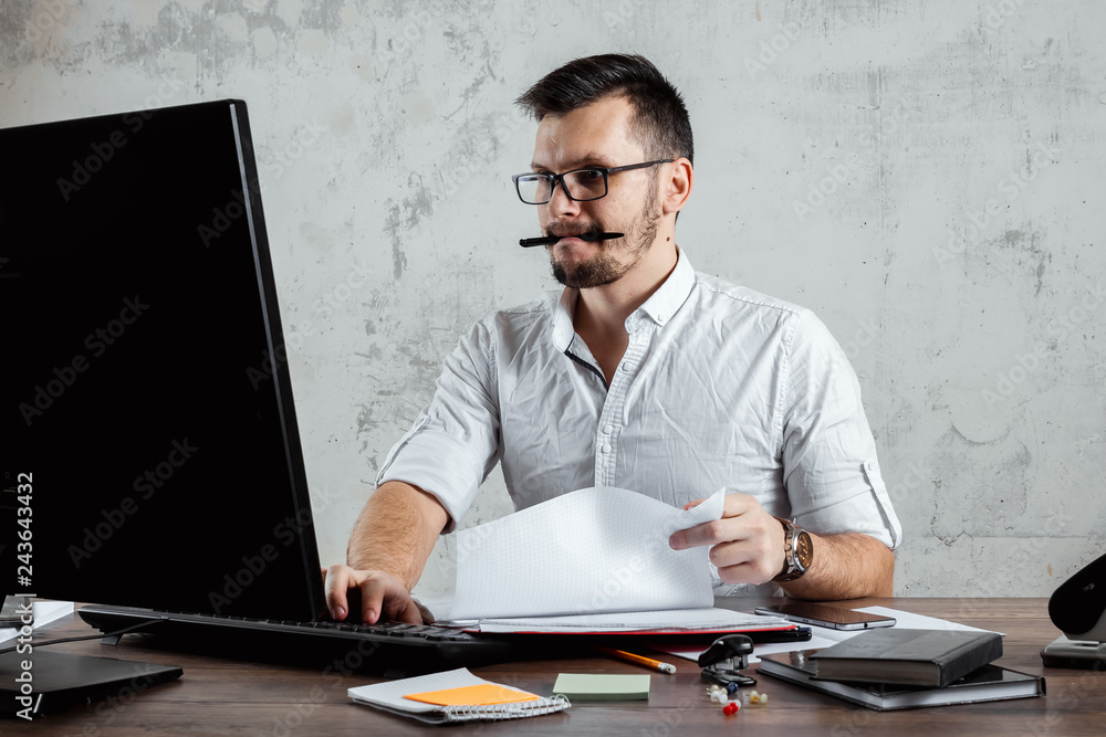 A man, a man sitting at a table in the office, working on a computer. The concept of office work. Copy space. A man, a man sitting at a table in the office, working on a computer. The concept of office work. Copy space.