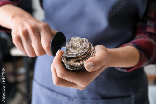 Woman opening raw oyster with knife, closeup photo