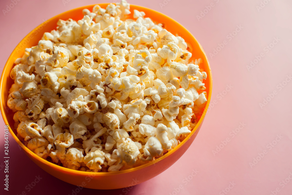 An orange bowl with popcorn isolated on pink background An orange bowl with popcorn isolated on pink background