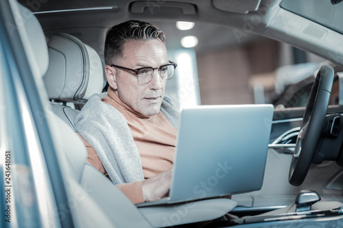 Busy prosperous businessman using his laptop sitting in car