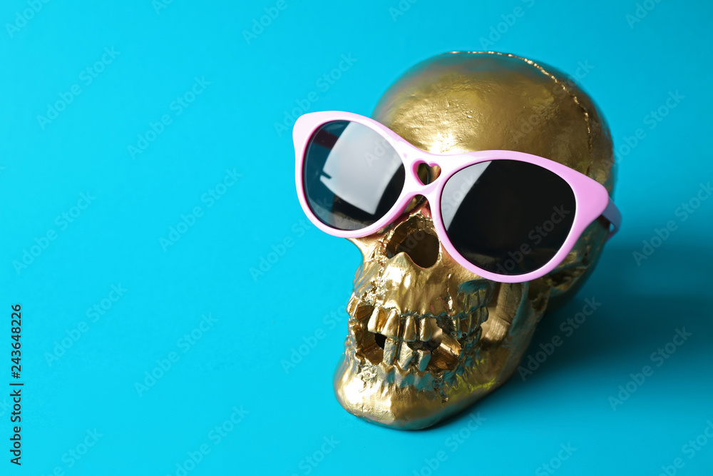 Golden human skull with sunglasses on color background Golden human skull with sunglasses on color background