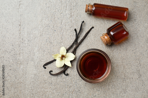 Glass bowl and bottles with vanilla extract on grey background photo