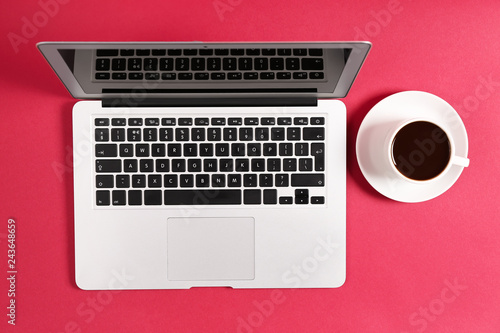 Modern laptop and cup of coffee on color background